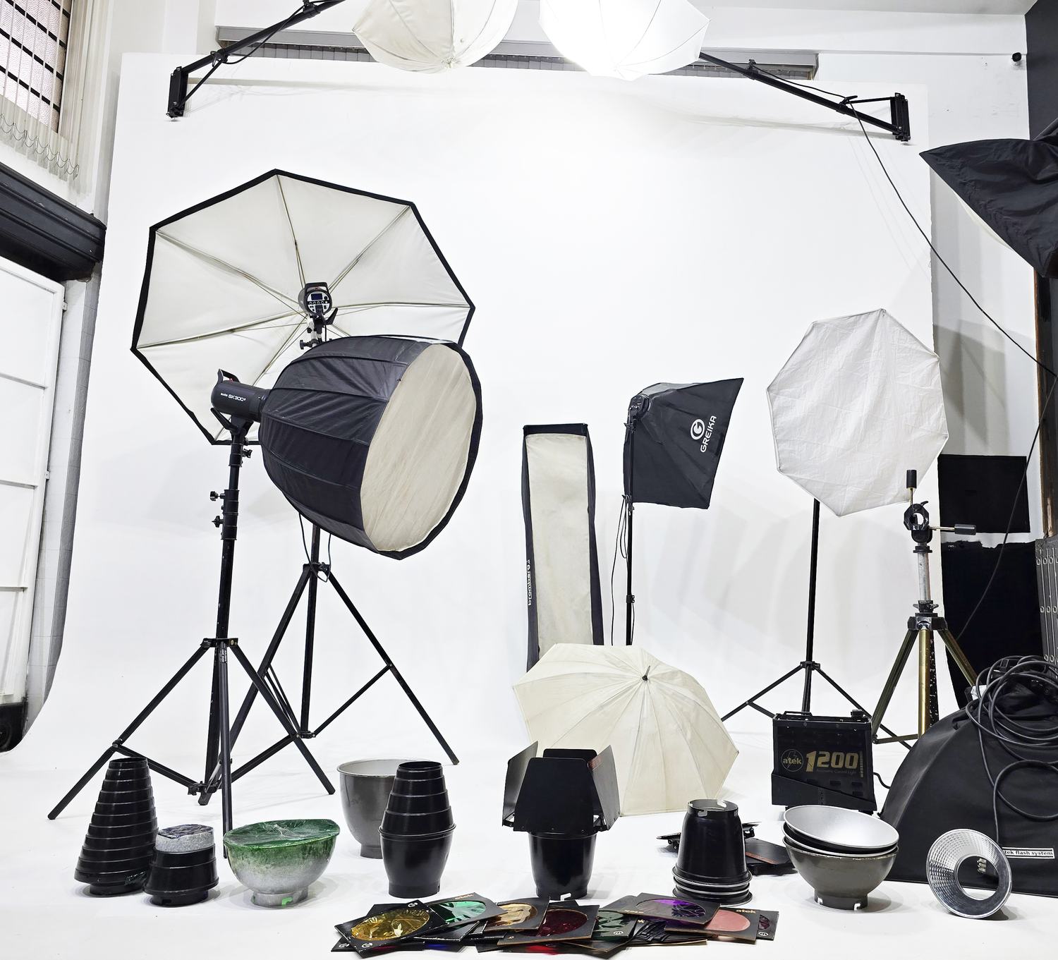 Equipamento de iluminação do Estúdio Lumiar montado sobre a ciclorama: flashes Godox, softbox parabólico, octabox, strip, sombrinhas, refletores, grids e gelatinas